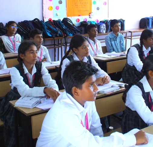 Students in uniform listening to a teacher.